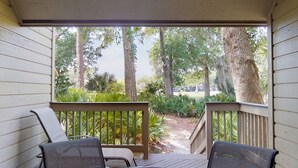 A covered porch with two chairs and a wooden railing, overlooking a garden with trees and a pathway. - Large Golf Course Villa with Lots of Space for Everyone! (Hilton Head)