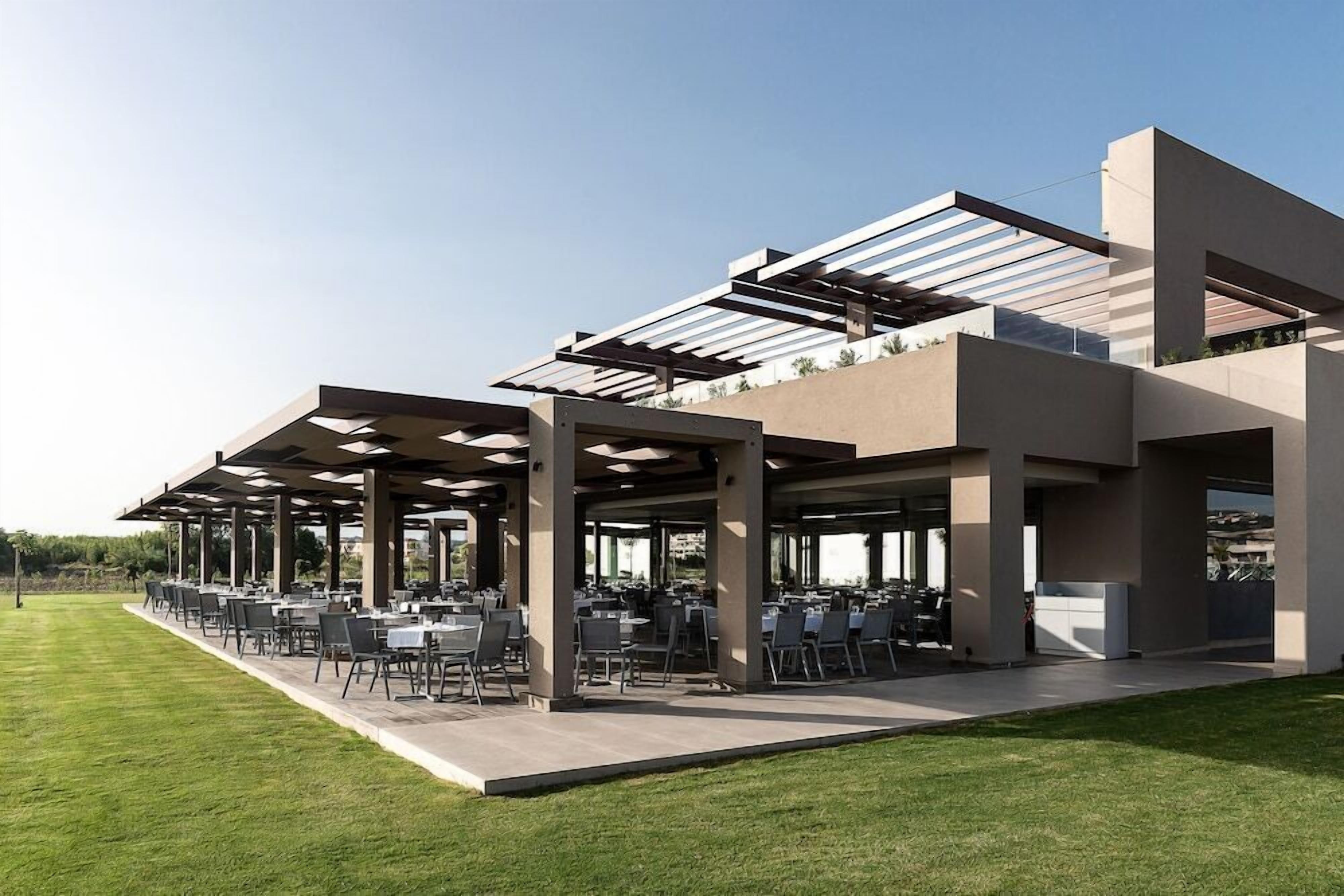 An outdoor dining area with tables and chairs under a modern structure with a glass roof.