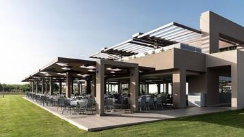An outdoor dining area with tables and chairs under a modern structure with a glass roof.