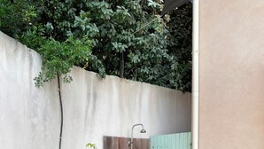 Zona exterior petita amb una planta de bambú, una escala de fusta, un vàter metàl·lic, una porta de fusta i un tub d'aigua per al jardí.