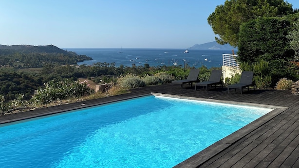 Una piscina amb un pont de fusta, dues gandules i vista al mar i a les muntanyes.