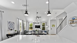 Une cuisine moderne dotée d’un grand îlot central, de luminaires suspendus et d’un coin repas avec un téléviseur.