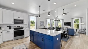 Une cuisine moderne avec des meubles blancs, un îlot central bleu, des appareils en acier inoxydable et des luminaires suspendus.