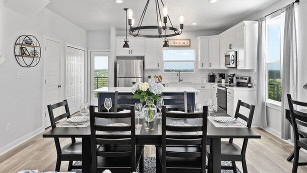 Une cuisine moderne avec des meubles blancs, un îlot central et un coin repas comprenant une table et des chaises noires.