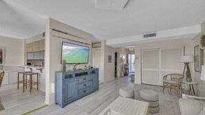 Uma sala de estar moderna com televisão de tela plana, um armário azul, uma área de jantar com mesa branca e uma cadeira de vime.