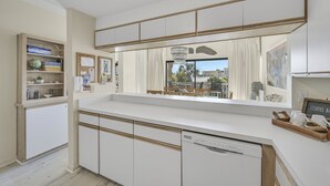 Cozinha moderna com armários brancos, máquina de lavar louça embutida e vista para um pátio externo.