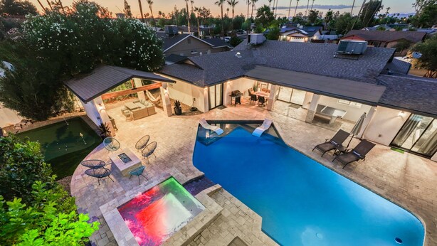 Patio trasero residencial con piscina, jacuzzi y zona de estar al aire libre con mobiliario.