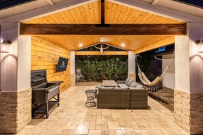 An outdoor patio with a wooden ceiling, a grill, wicker furniture, and a hammock.