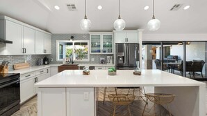Una cocina moderna con armarios blancos, una isla grande e iluminación colgante.