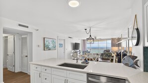 A modern kitchen with a large island, stainless steel dishwasher, and a view to the living area.