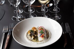 A white plate with a fish dish, garnished with herbs and vegetables, on a dark table. - Peak 12 Design Hotel (Viborg)