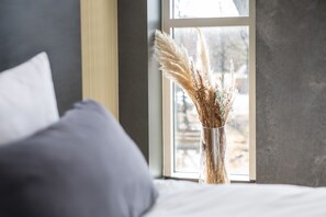A bedroom with a large window, a bed with white bedding, and a vase with dried plants. - Peak 12 Design Hotel (Viborg)