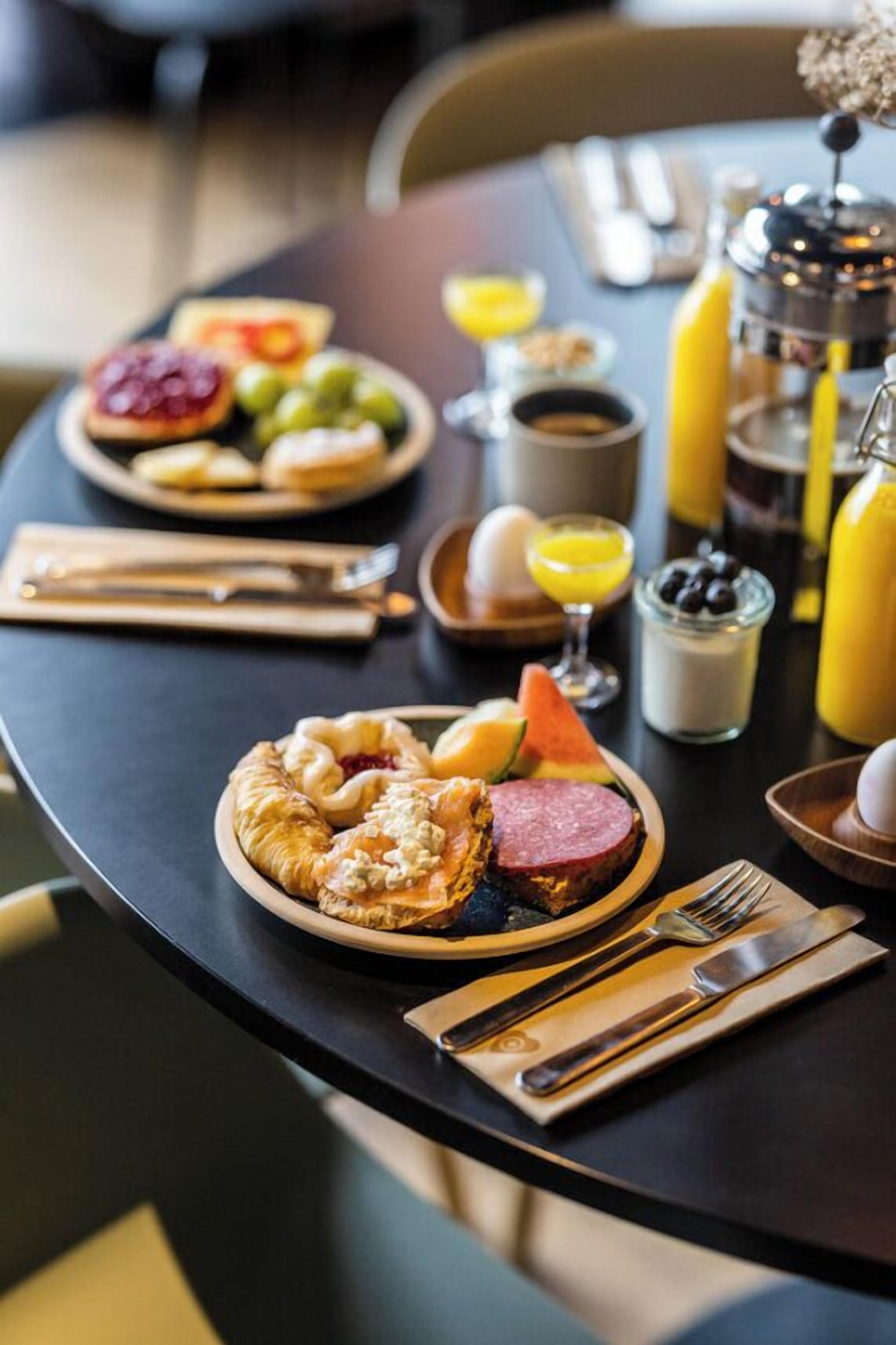 Een ontbijttafel met borden eten, een koffiepot en een fles sinaasappelsap.