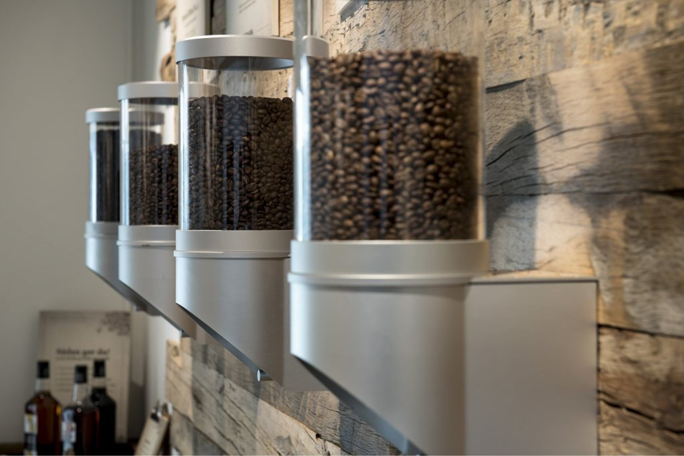 A row of cylindrical containers with different contents, likely coffee beans, on a wall with a rustic stone texture.