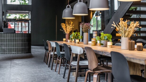 A modern dining area with a long wooden table, black and white chairs, and hanging pendant lights. - Peak 12 Design Hotel (Viborg)