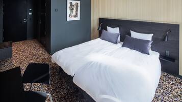 A hotel room with a large bed, a headboard, a wall-mounted lamp, and a carpeted floor.