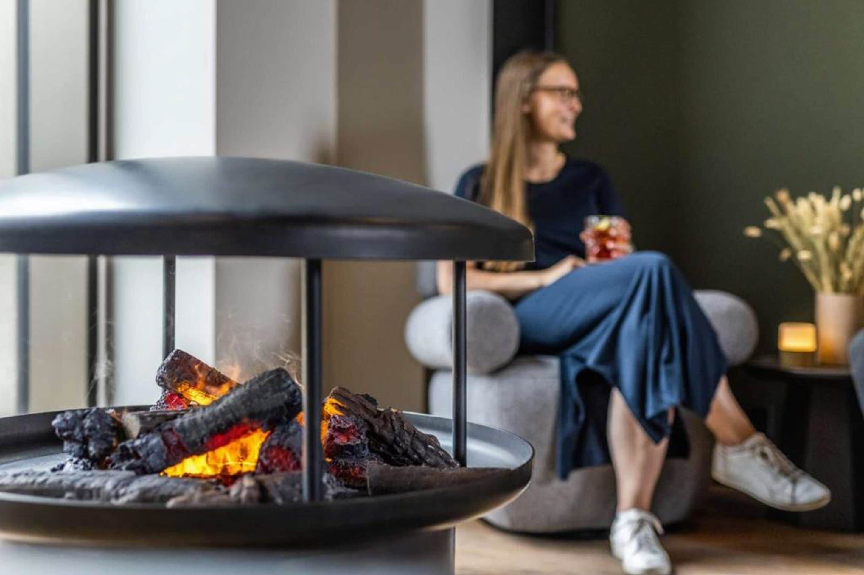 A modern interior with a charcoal fire feature and a person sitting on a grey sofa.