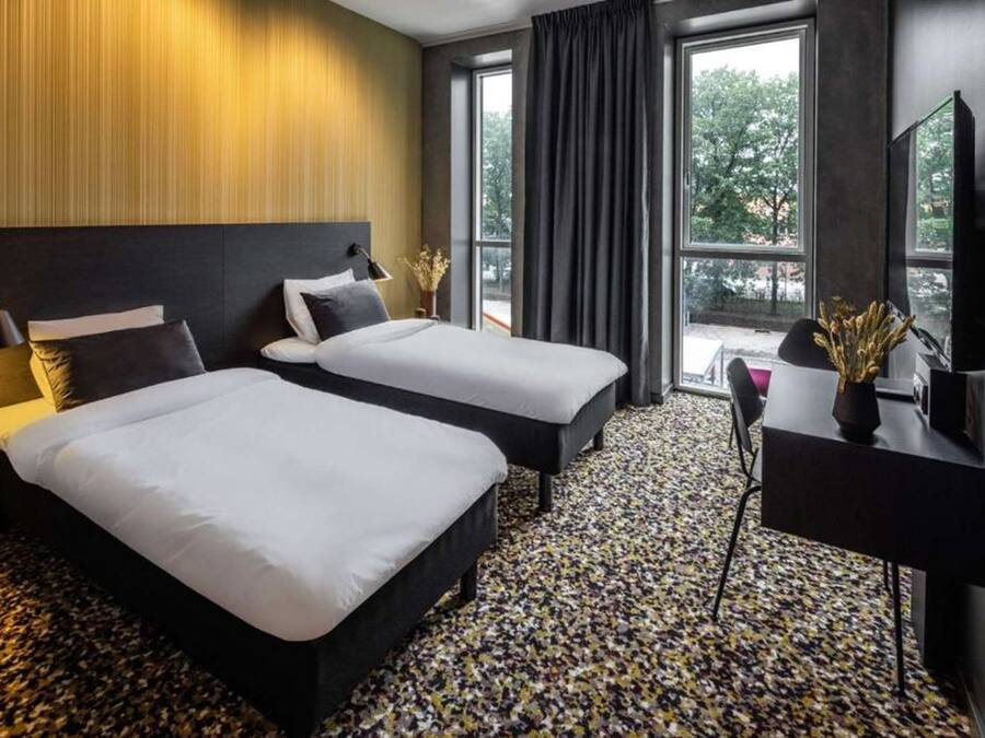 A hotel room with two beds, a desk, and a large window with curtains.