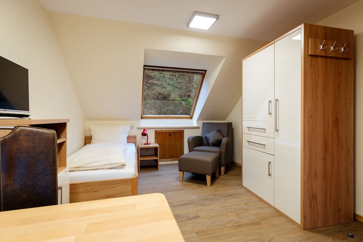 Une pièce de taille modeste comprenant un lit, un bureau, une chaise, une armoire et un puits de lumière.