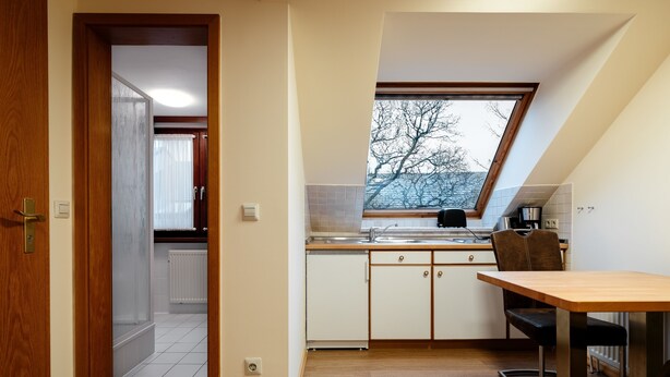 A kitchen with a skylight, white cabinets, a wooden table, and a view of trees outside. - Haus Frier (Helgoland)