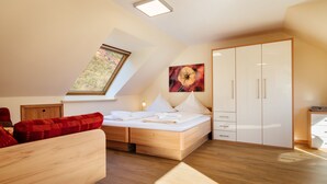 A modern bedroom with a skylight, a bed with white linens, a red patterned sofa, and a wardrobe. - Haus Frier (Helgoland)