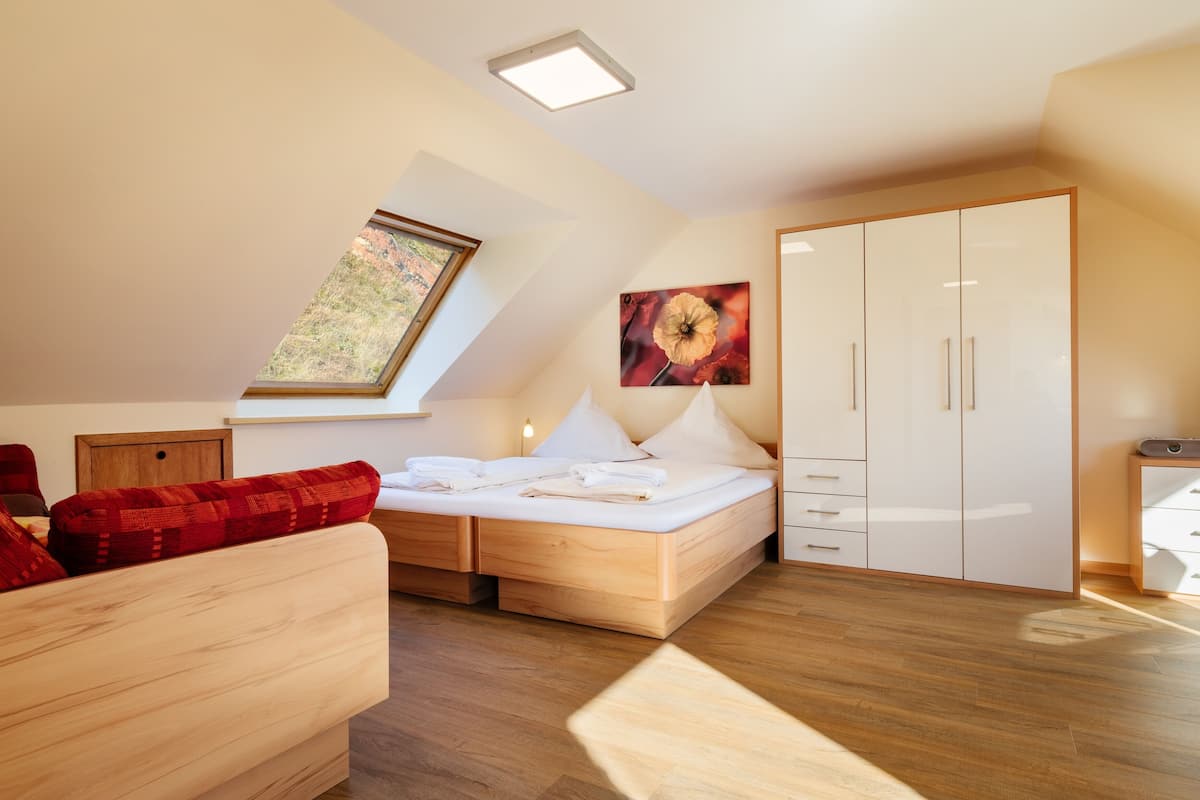 Une chambre à coucher moderne avec une lucarne, un lit recouvert de draps blancs, un canapé rouge à motifs et une armoire.