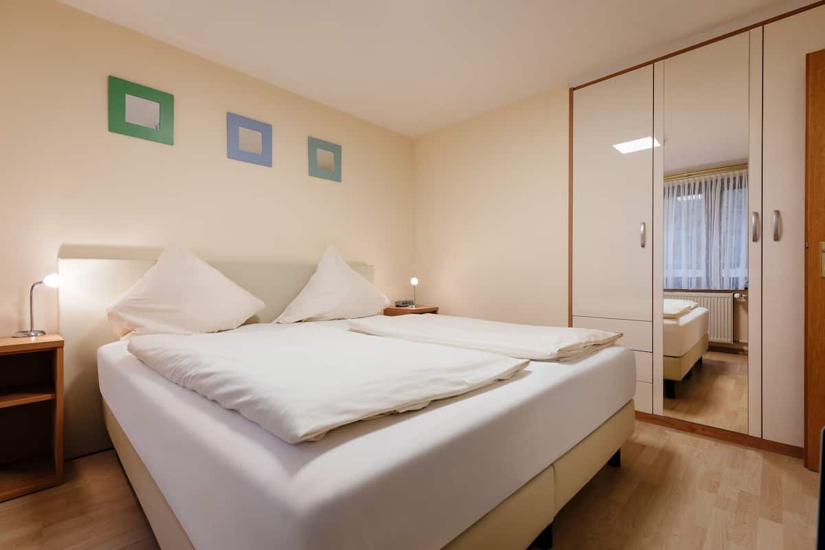 Un lit double avec du linge de lit blanc, une table de chevet avec une lampe et un miroir au mur.