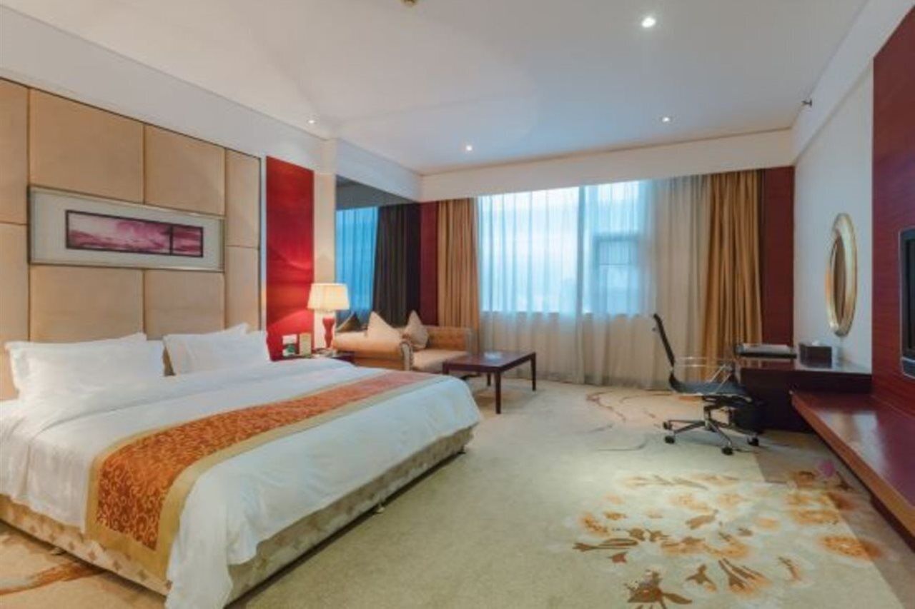 A hotel room with a large bed, a desk, a chair, and a TV.