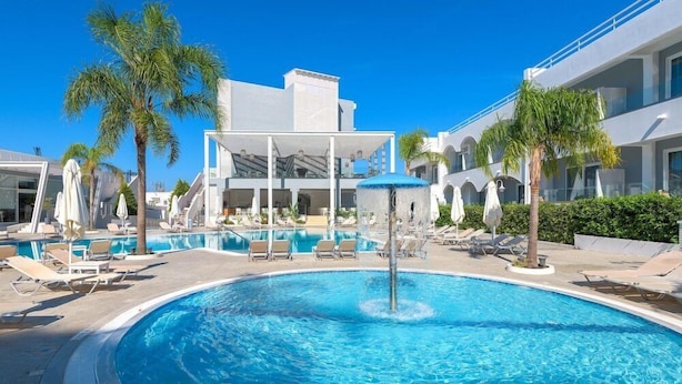 A swimming pool with lounge chairs and umbrellas, surrounded by palm trees and modern buildings. - Oceanis Park Hotel (Rhodes)