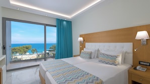 A modern hotel room with a large bed, a wooden headboard, a nightstand with a phone, and a view of the sea through a sliding glass door. - Oceanis Park Hotel (Rhodes)