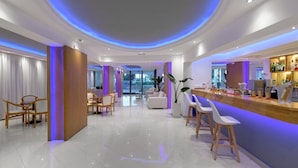 A modern hotel lobby with a bar area, seating, and a view of the outdoors. - Oceanis Park Hotel (Rhodes)