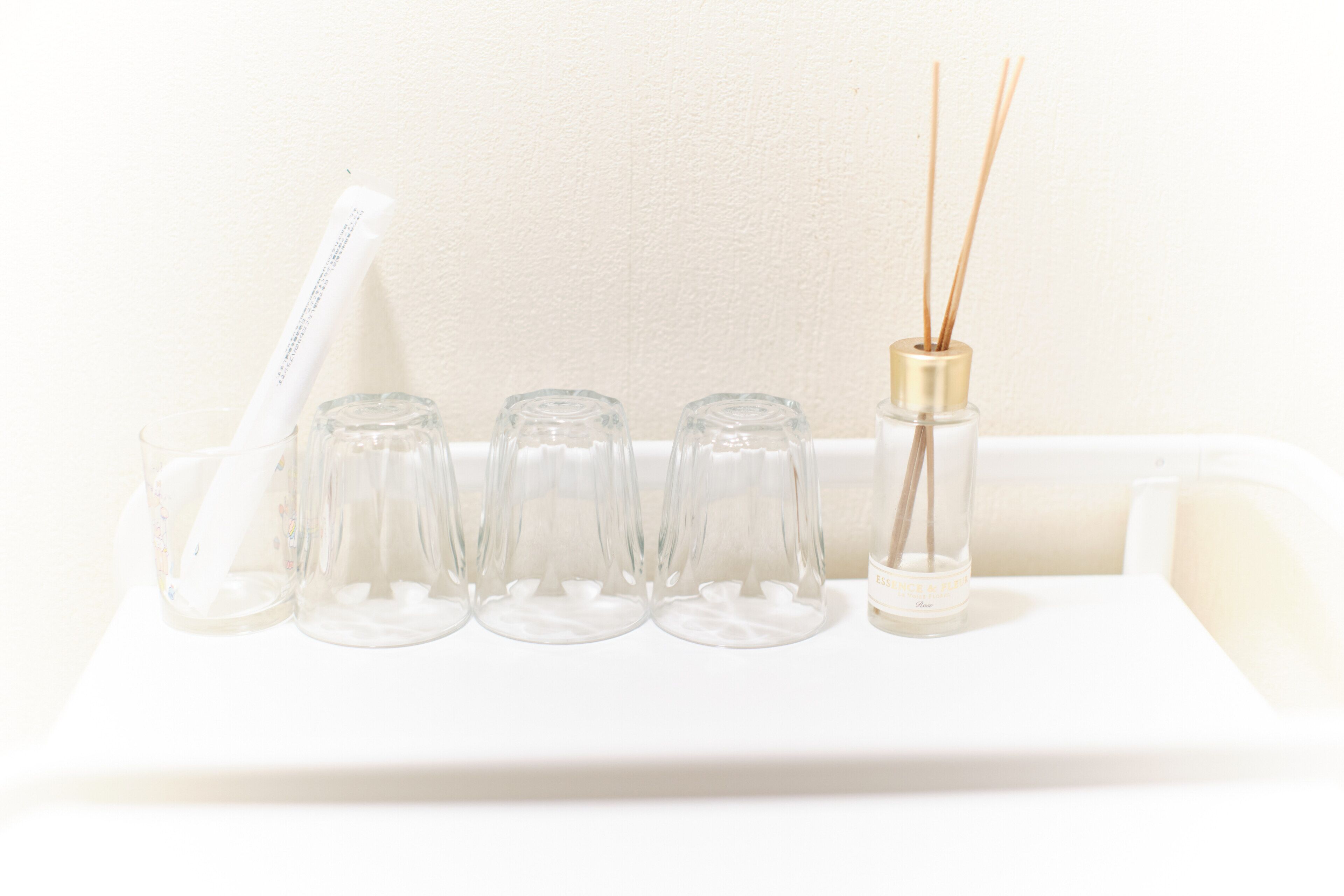 Un plateau blanc avec quatre verres transparents et une bouteille contenant des tiges de roseau.