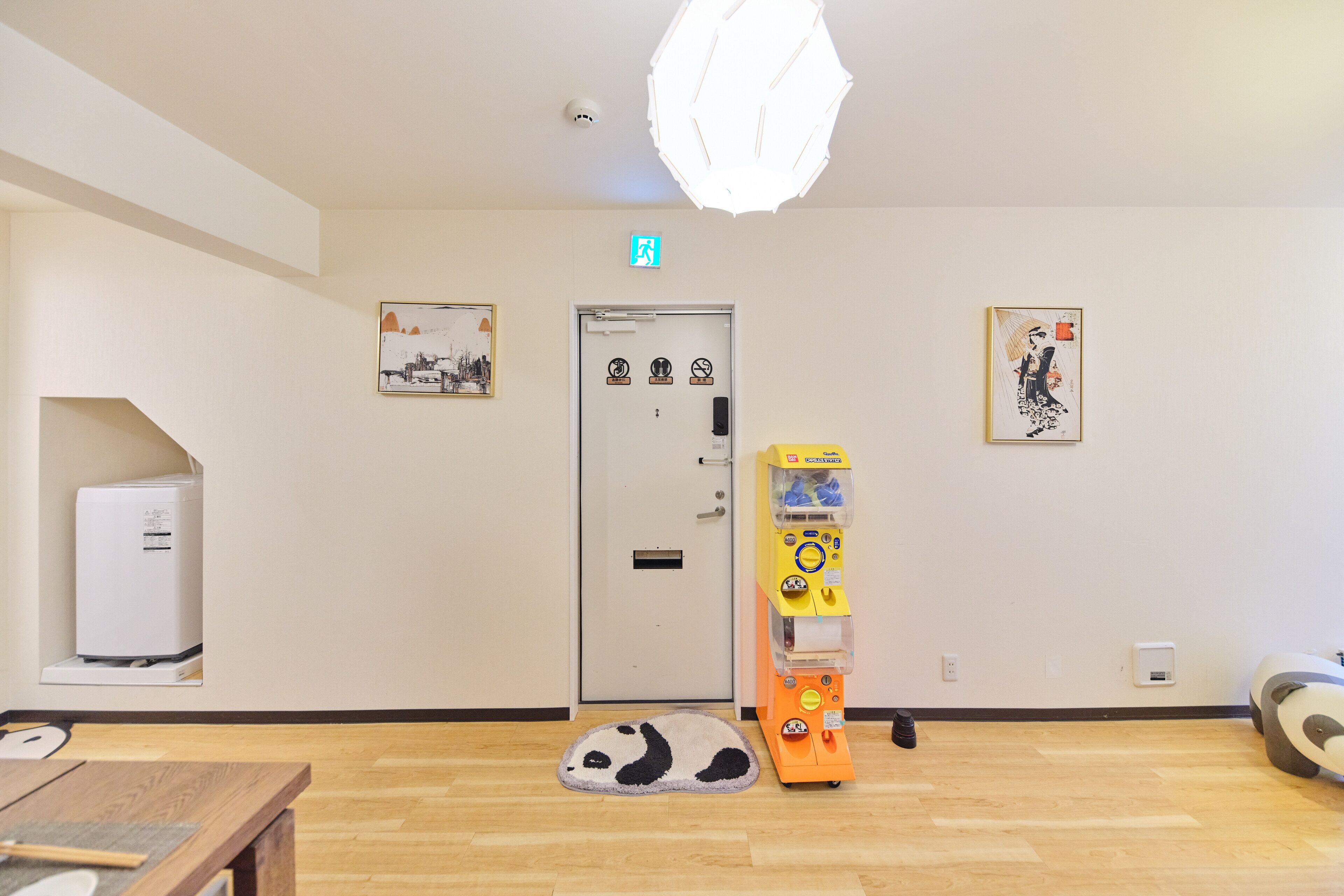 A room with a wooden floor, a panda-themed rug, a vending machine, and a door with a security camera.