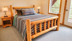 Een houten bed met een bedovertrek met patroon, twee nachtkastjes met lampen, en een raam met uitzicht op groen.