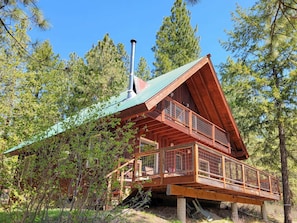 A cabin with a metal roof, wooden deck, and a chimney.