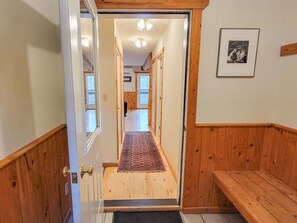 Un pasillo con paredes de madera, un banco y un tapete que conduce a una habitación.