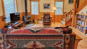 Een gezellige woonkamer met een open haard, een televisie, een bank, een fauteuil, een boekenkast en een trap.