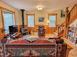 Una sala de estar acogedora con chimenea, televisor, sofá, sillón, estantería y una escalera.