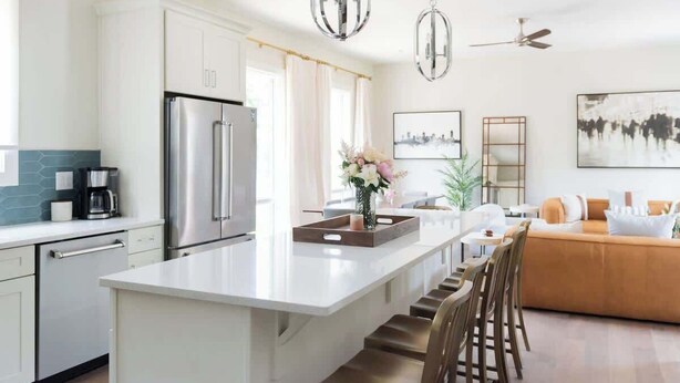 A modern kitchen with a central island, stainless steel appliances, and a dining area with a sofa and chairs. - Spacious 4BR, Rooftop Patio, Garage, Walk to Faves |  5 Mins to Nissan Stadium, Less than 10 Mins to Broadway, 24 Hr Hospitality, Great for Groups (Nashville)