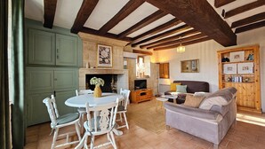 A cozy living room with a fireplace, wooden beams, a dining area with white chairs, and a grey sofa. - 2 Gites 8 Personnes Proche Beauval et Chenonceaux (Montrichard Val de Cher)