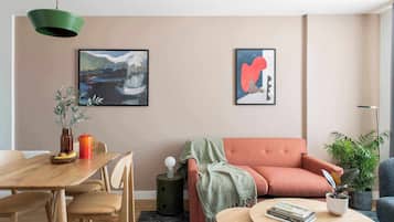 A modern living room with a wooden dining table, a sofa, and two framed abstract paintings on the wall.