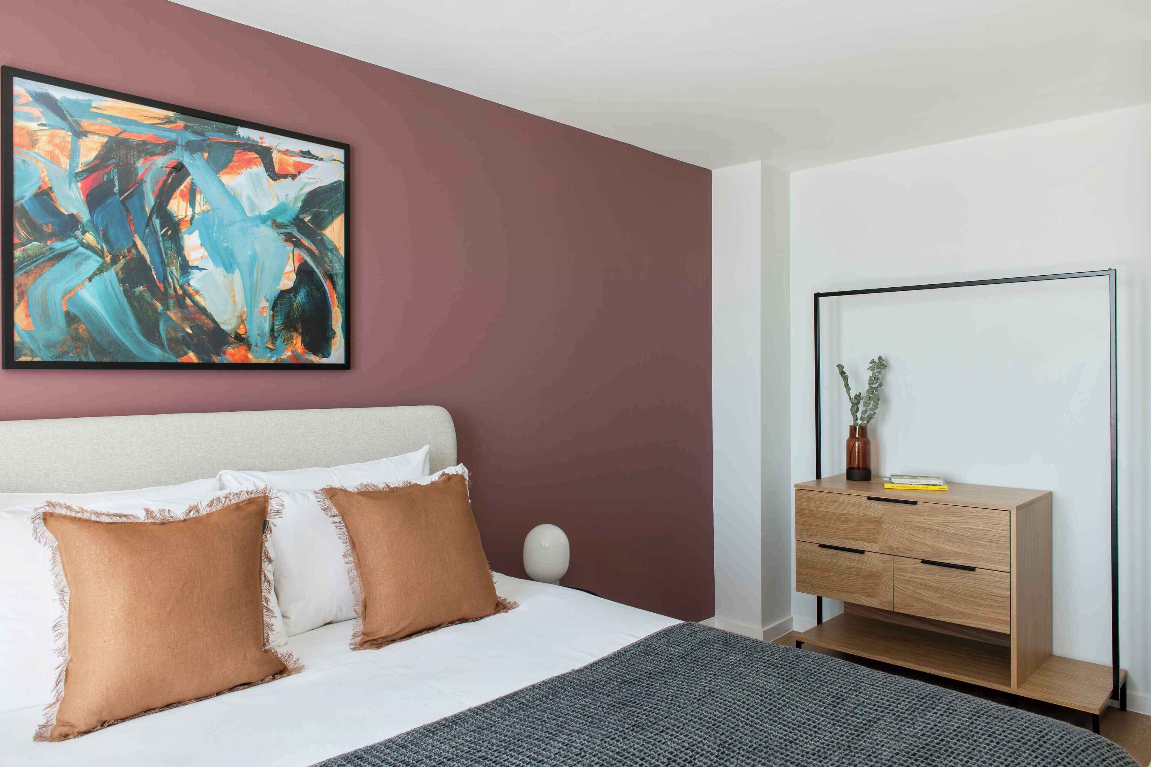 Een moderne slaapkamer met een bed, een nachtkastje, een dressoir en een groot abstract schilderij aan de muur.