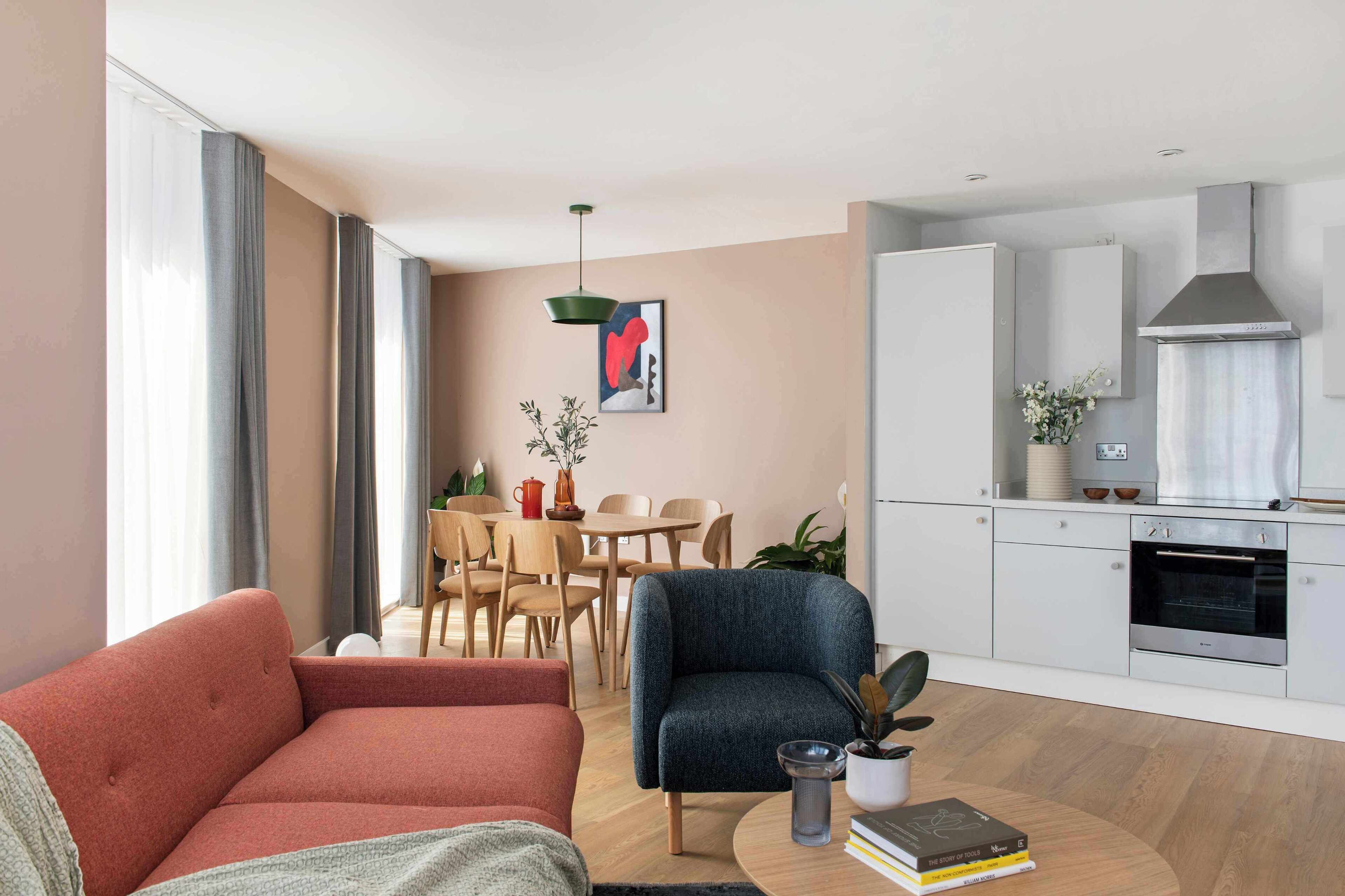 Uma sala de estar moderna com sofá, área de jantar com cadeiras e mesa, e cozinha com armários e forno.