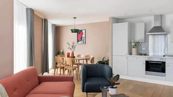 Een moderne woonkamer met een bank, een eethoek met stoelen en een tafel, plus een keuken met kasten en een oven.