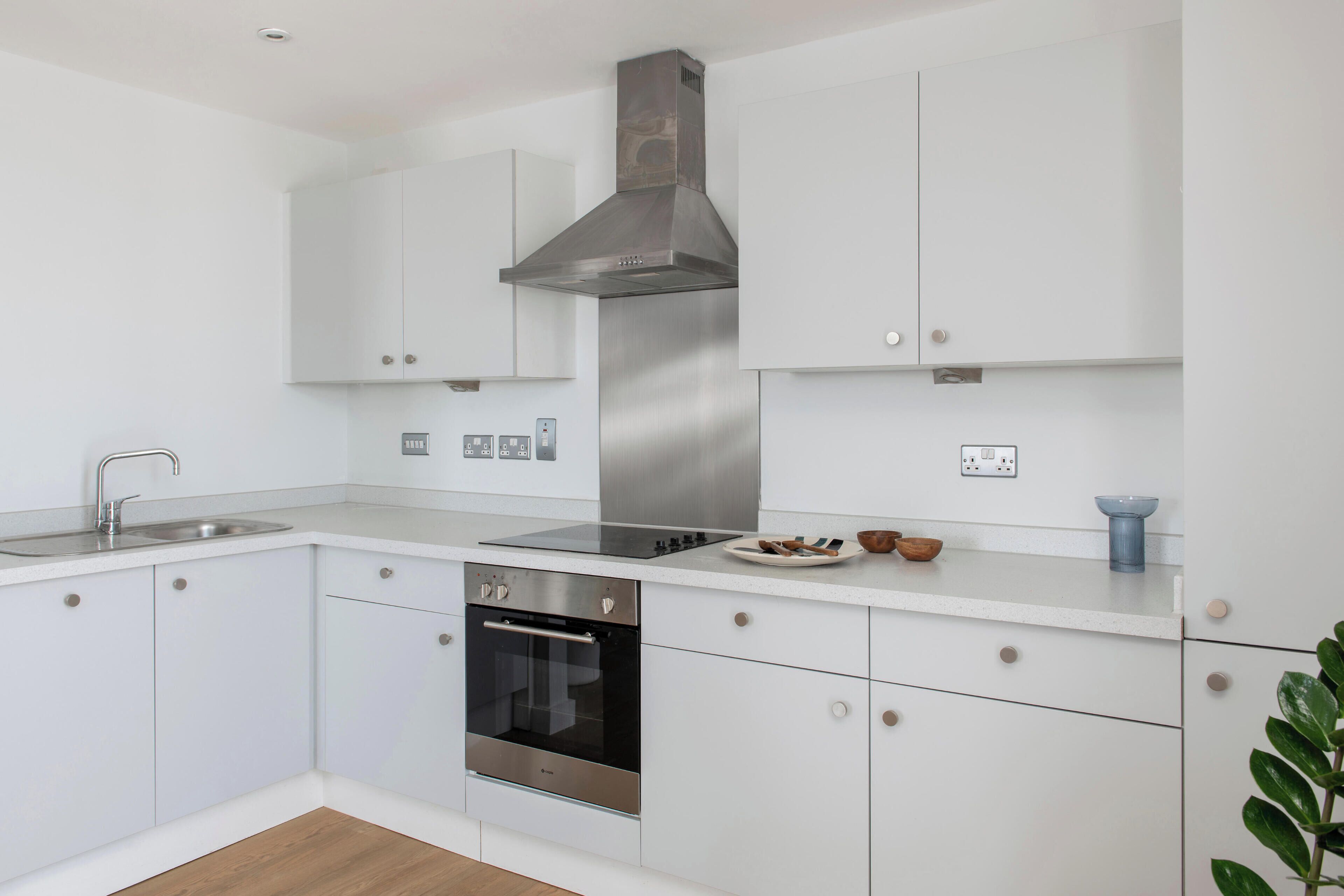 Una cocina moderna con armarios blancos, electrodomésticos de acero inoxidable y horno empotrado.