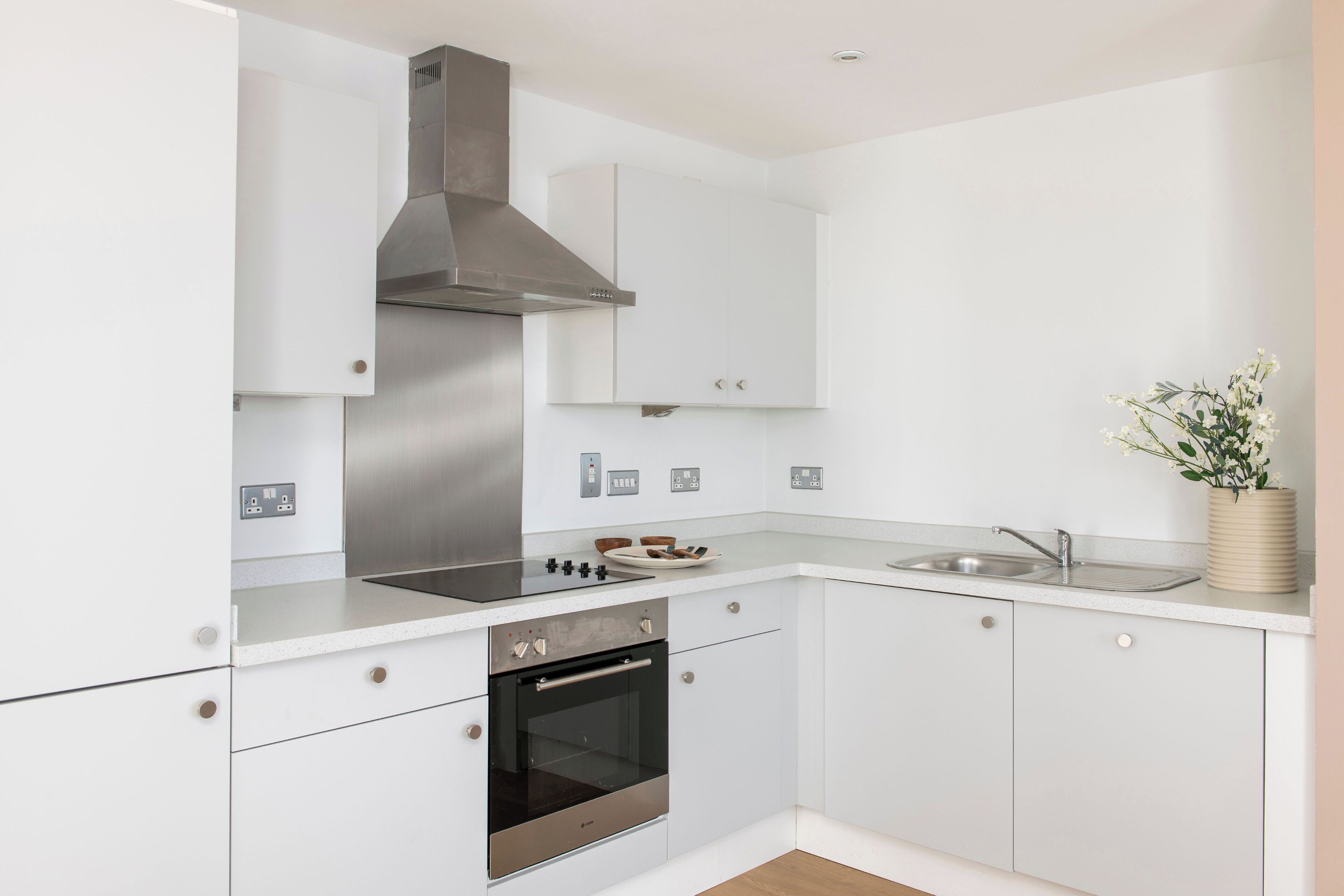 A modern kitchen with white cabinetry, stainless steel appliances, and a built-in oven.