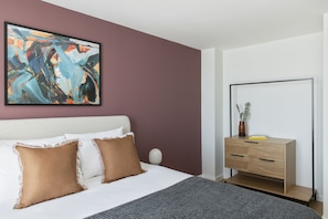 A modern bedroom with a bed, a dresser, and a large abstract painting on the wall. - Cove Paradise Street (Liverpool)