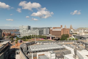 A cityscape with modern buildings, a waterfront, and a large open plaza with a unique roof structure.