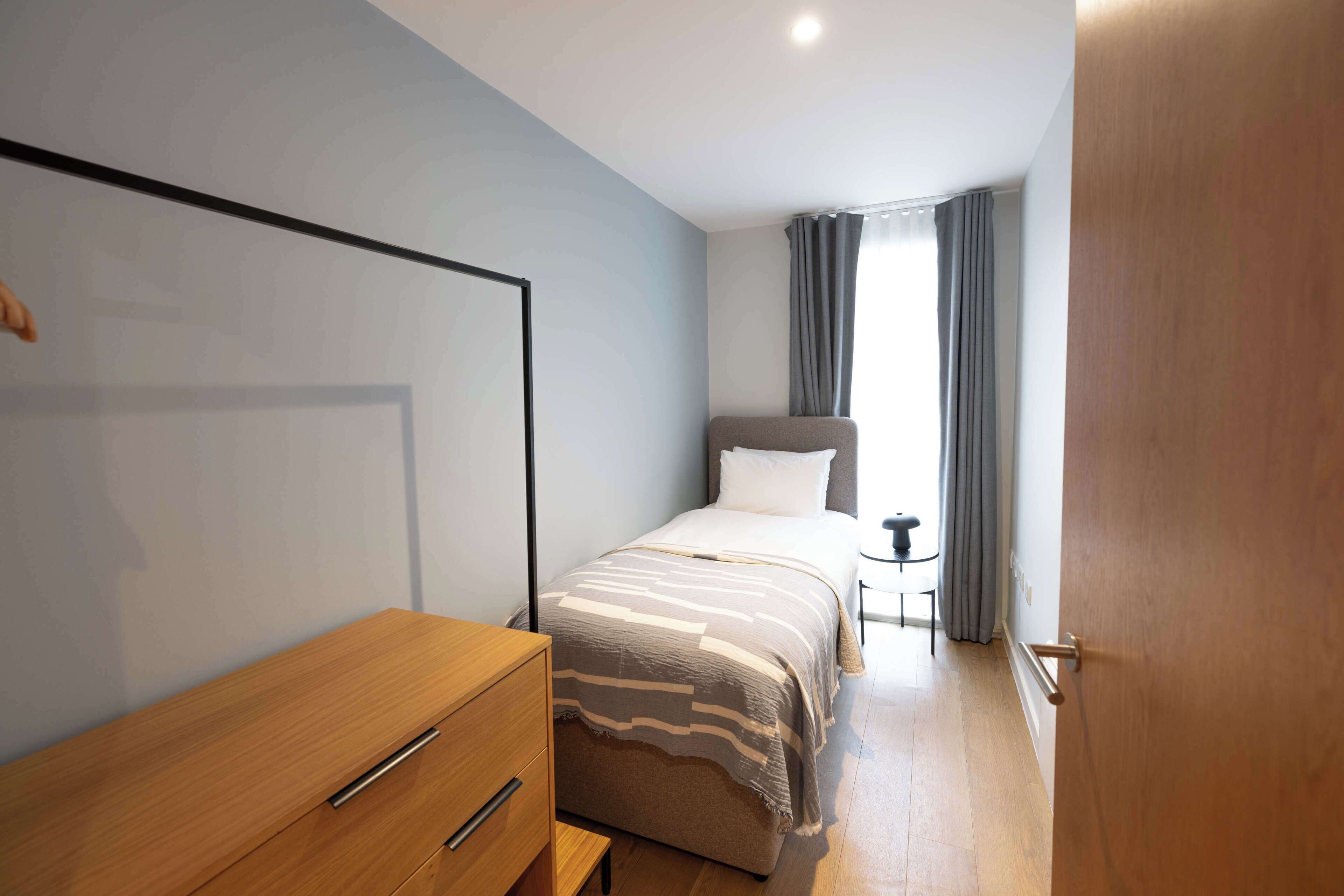 Une chambre d’hôtel avec un lit, une commode en bois, une petite table et une fenêtre avec des rideaux.