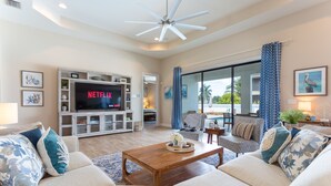 Un salón amplio con un televisor de pantalla plana grande, asientos cómodos y un ventilador de techo.